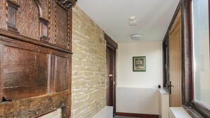 A narrow hallway with stone walls, wooden paneling, and a door with a glass panel. - Walton Maisonette (Craven Arms)