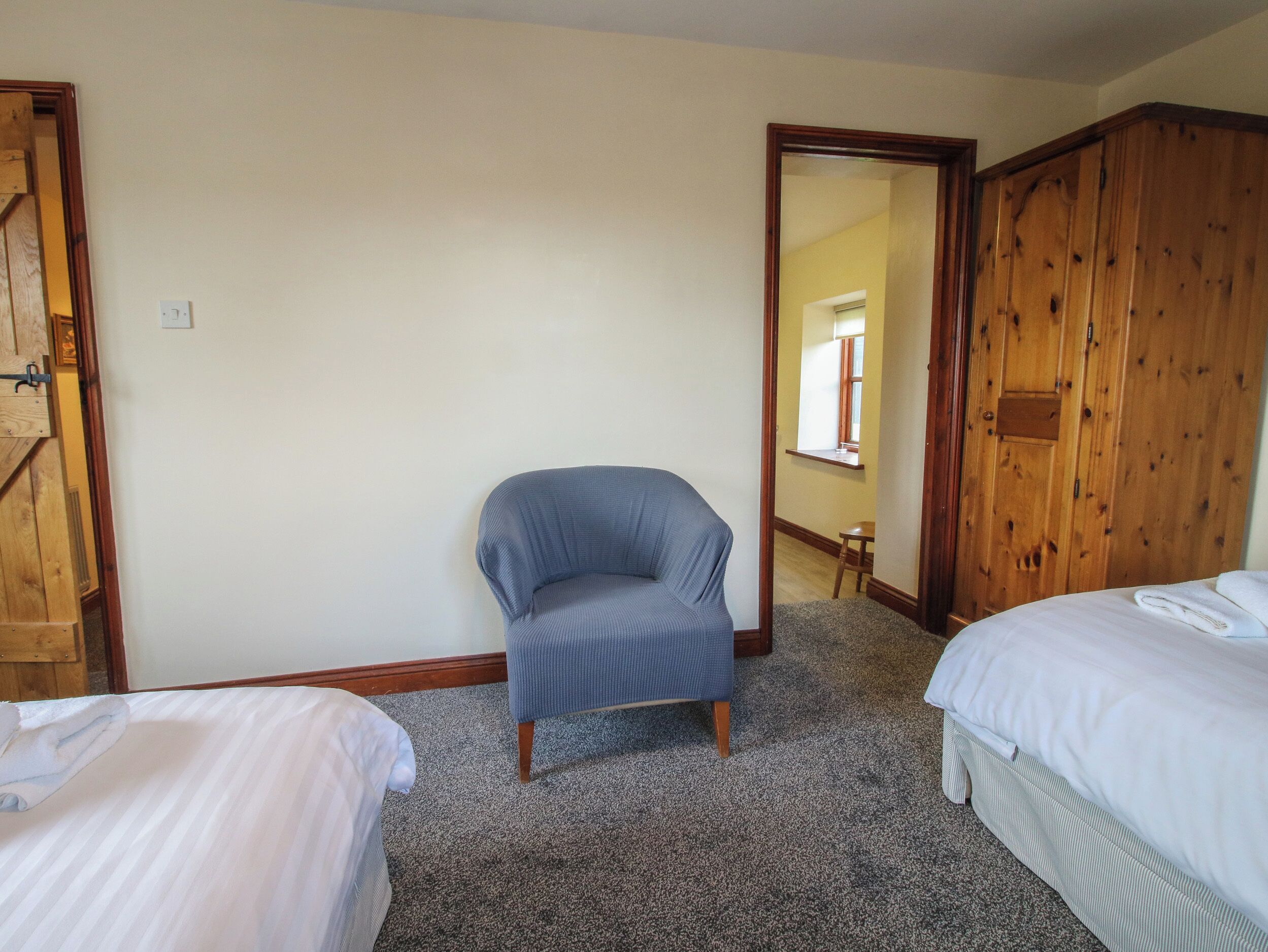 A bedroom with two beds, a blue armchair, and wooden wardrobes.