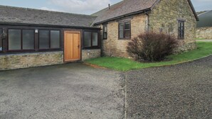 A stone building with a wooden door, large windows, and a gravel driveway. - Walton Maisonette (Craven Arms)