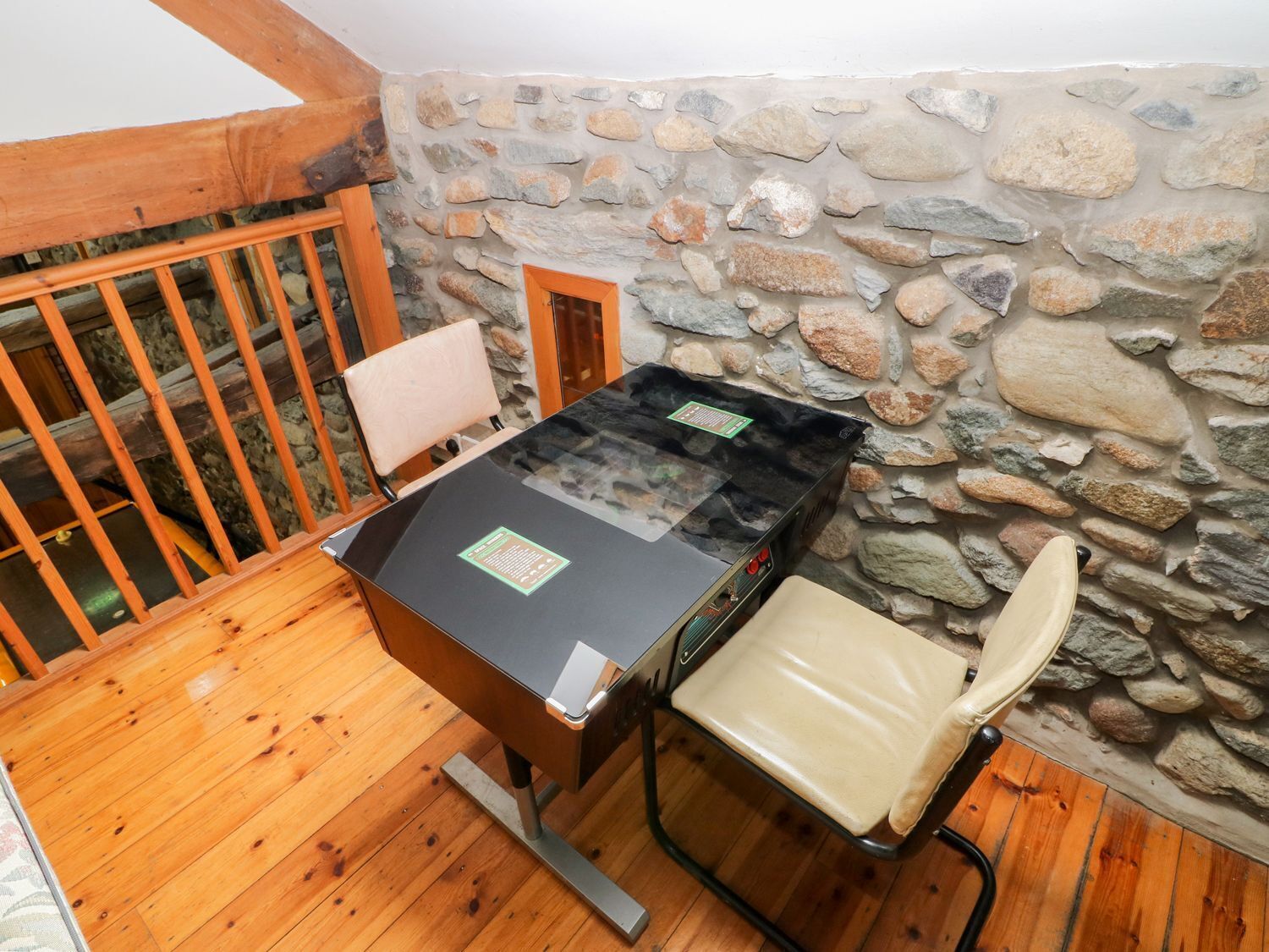 A wooden dining table with a black top, a chair with a beige cushion, and a stone wall in the background.