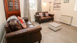 A living room with a brown leather sofa, a matching ottoman, a wooden cabinet, and a radiator. - Y Bwthyn (Pwllheli)