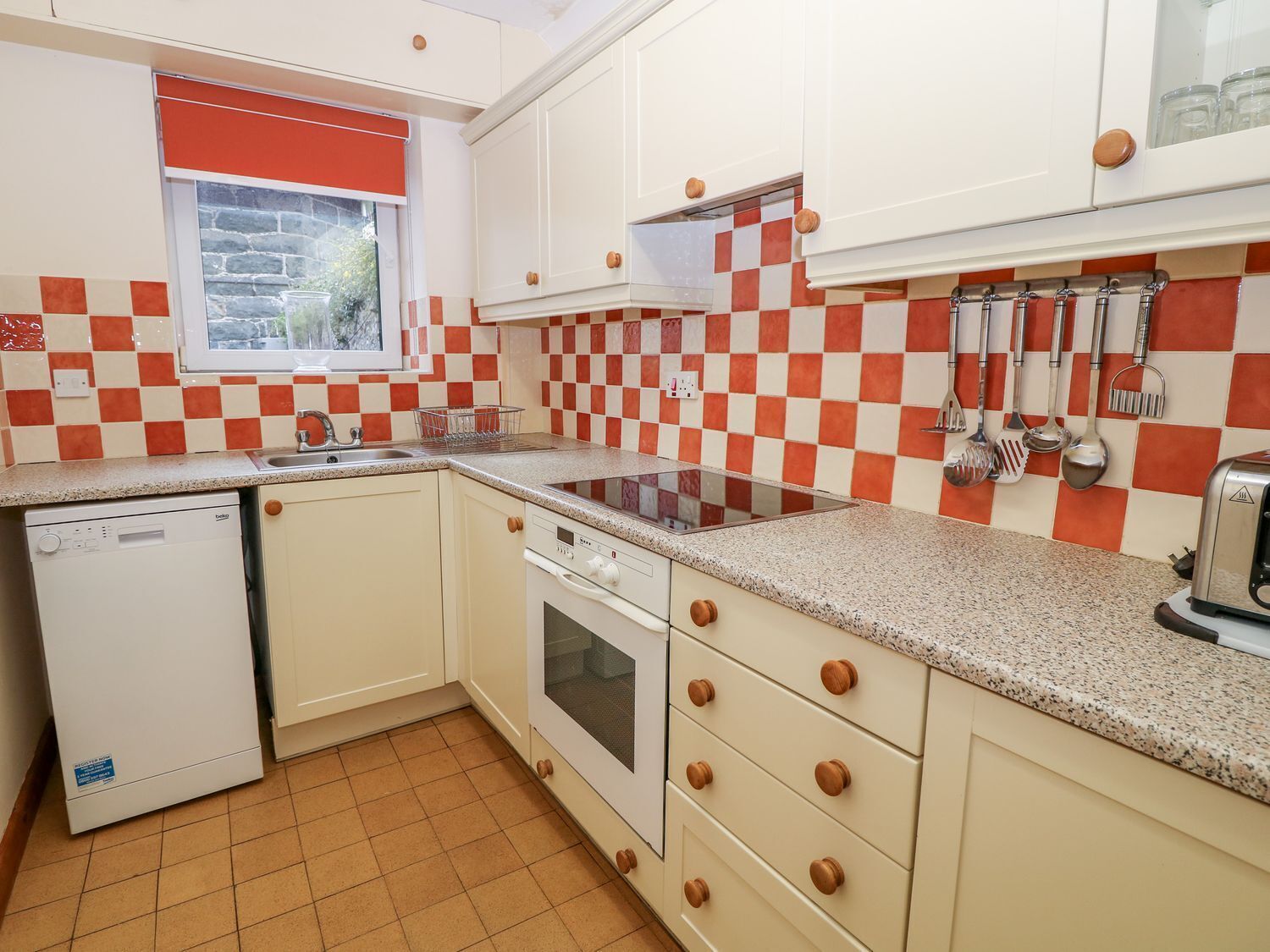 A compact kitchen with white cabinets, a red and white checkered backsplash, a built-in oven, and a dishwasher.