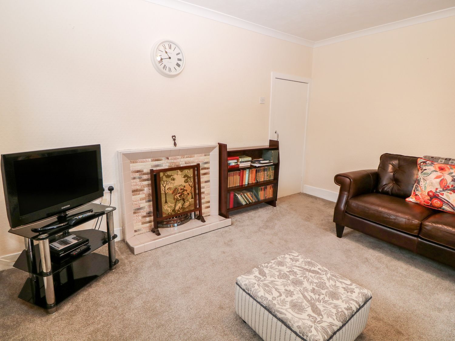 A living room with a flat-screen TV, a fireplace, a bookshelf, a leather couch, and a clock on the wall.