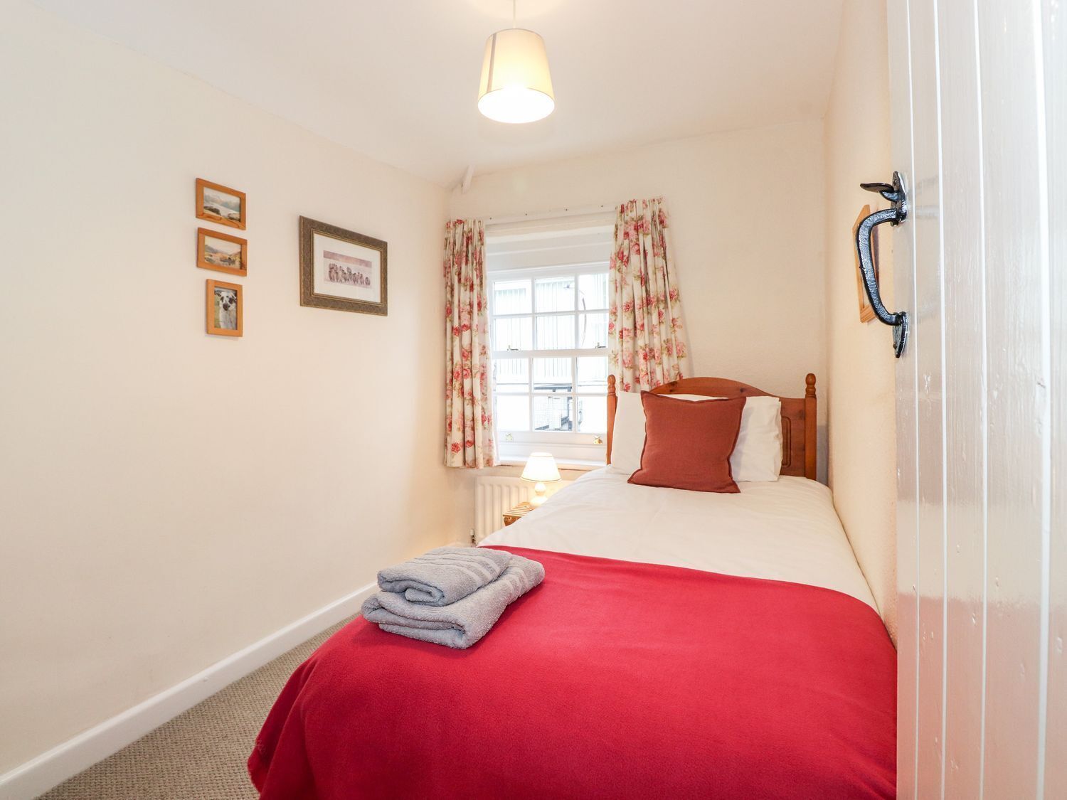 A bedroom with a bed, a window with curtains, a radiator, and a wall-mounted lamp.