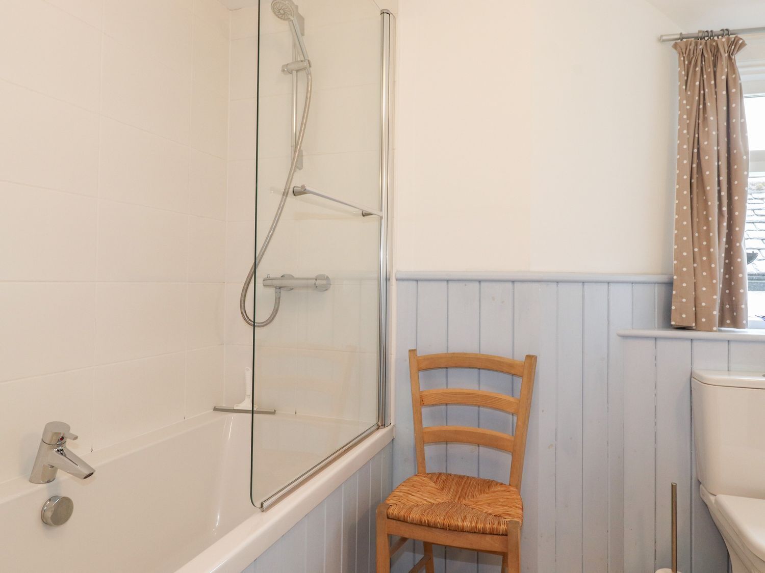 A bathroom with a bathtub, shower, and a wooden chair.