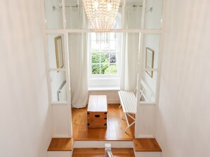 A staircase leading to a room with a wooden floor, a white bench, and a large window with a view of greenery. - Middletown (Keswick)