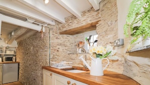 Une cuisine avec un mur en pierre, un plan de travail en bois et un meuble blanc doté de poignées en bois.