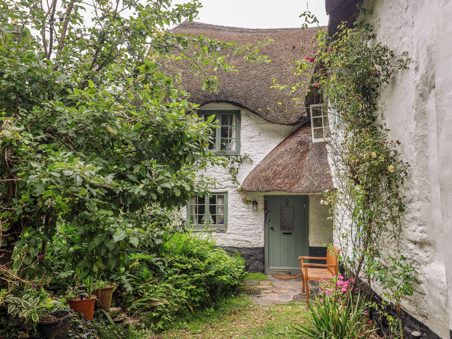 A quaint cottage with a thatched roof, a wooden bench, and a small garden area.