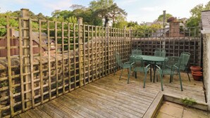 Una terraza de madera con una mesa y sillas, una cerca de madera y un muro de piedra al fondo.