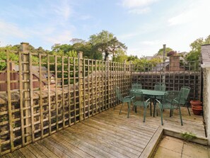 A wooden deck with a table and chairs, a wooden fence, and a stone wall in the background. - The Fir Grove Annex (Menai Bridge)