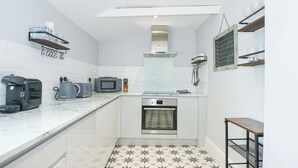 Cocina compacta con microondas, tostadora y horno. Cuenta con armarios blancos y un piso con diseño.