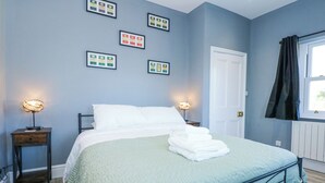 Un dormitorio ordenado con una cama, lámparas de noche y certificados enmarcados en la pared.