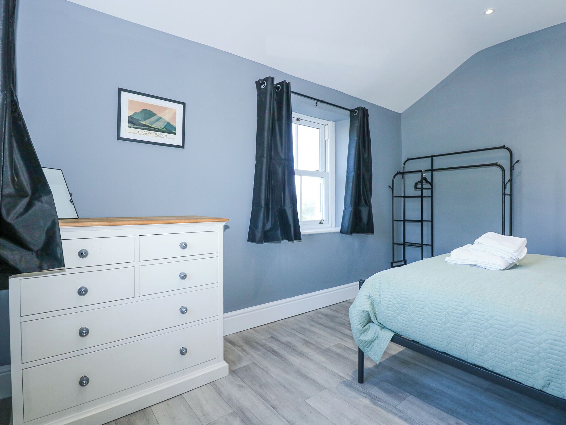 A bedroom with a bed, a dresser, a window with curtains, a metal bed frame, and a picture on the wall.