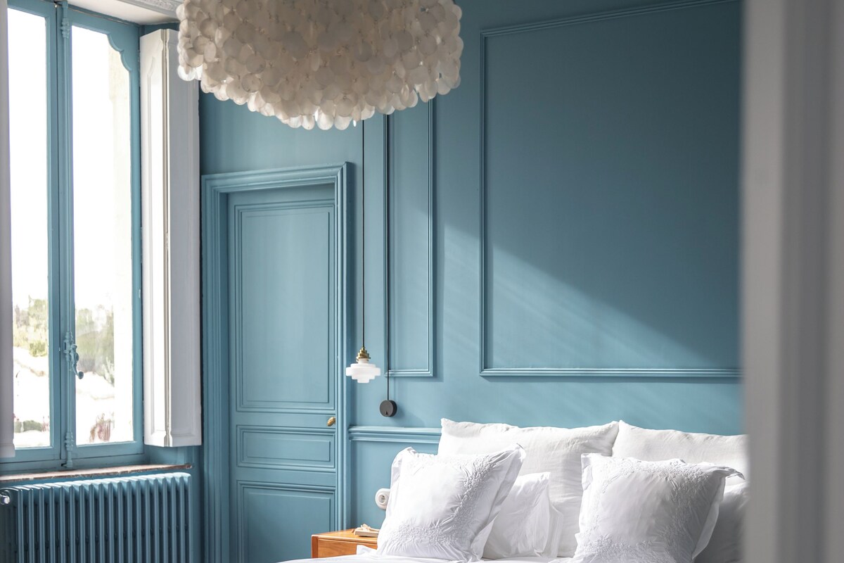 A bedroom with a bed, a hanging light fixture, a radiator, and a window.
