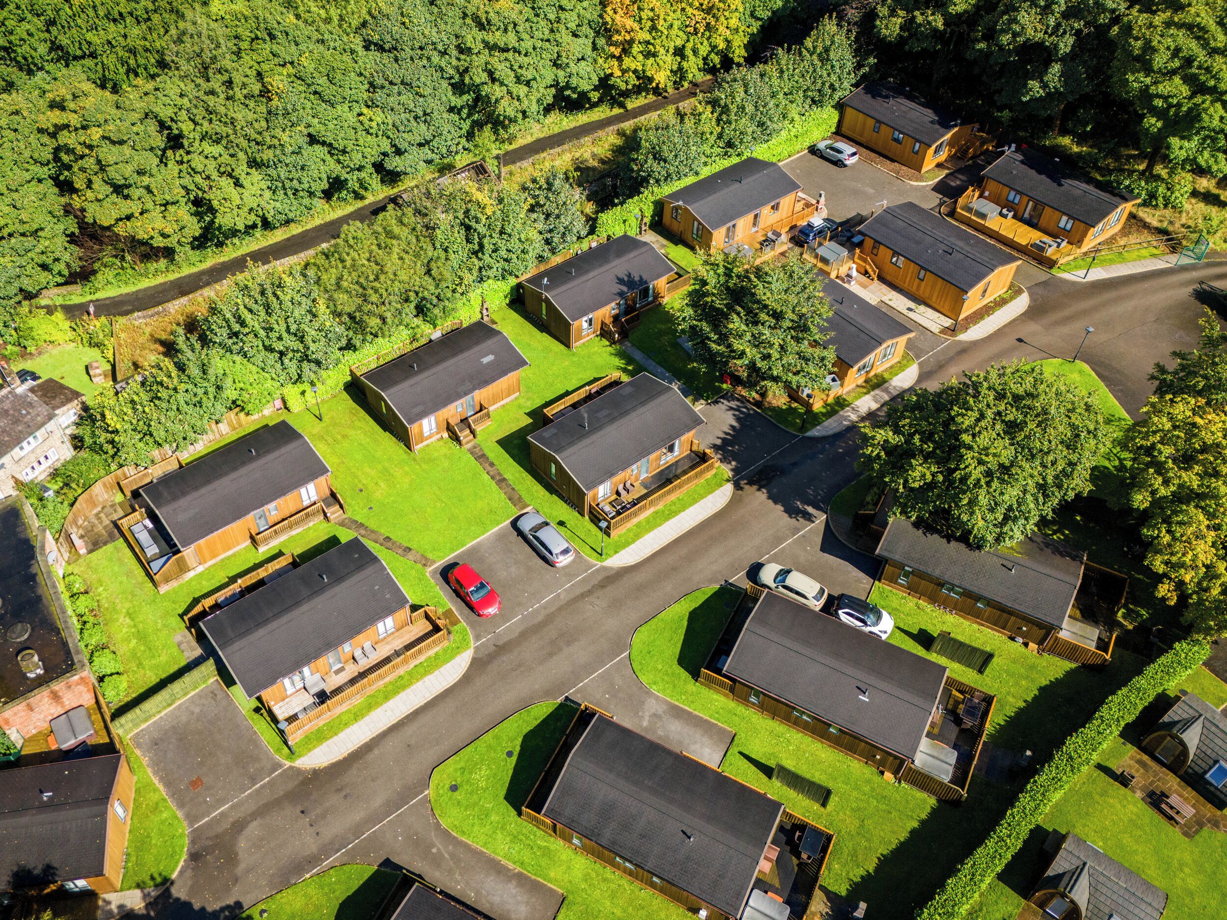 Vista aerea di una zona residenziale con diverse case di legno, ognuna con un tetto particolare, circondate da prati verdi.
