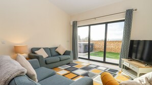 A modern living room with a sofa, armchair, and TV stand. - Bears Court Barn 1 (Cheltenham)
