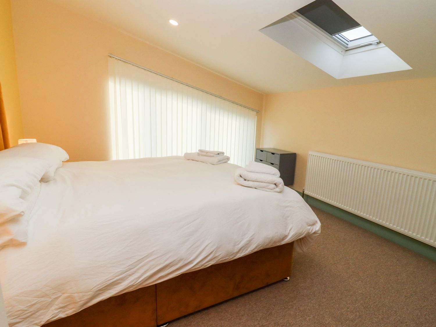 A bedroom with a bed, a radiator, a window with blinds, and a small cabinet.