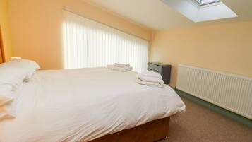 A bedroom with a bed, a radiator, a window with blinds, and a small cabinet.