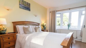 A neatly arranged bedroom with a wooden bed, bedside tables, and a window with curtains. - Castle View Lodge (Ilfracombe)
