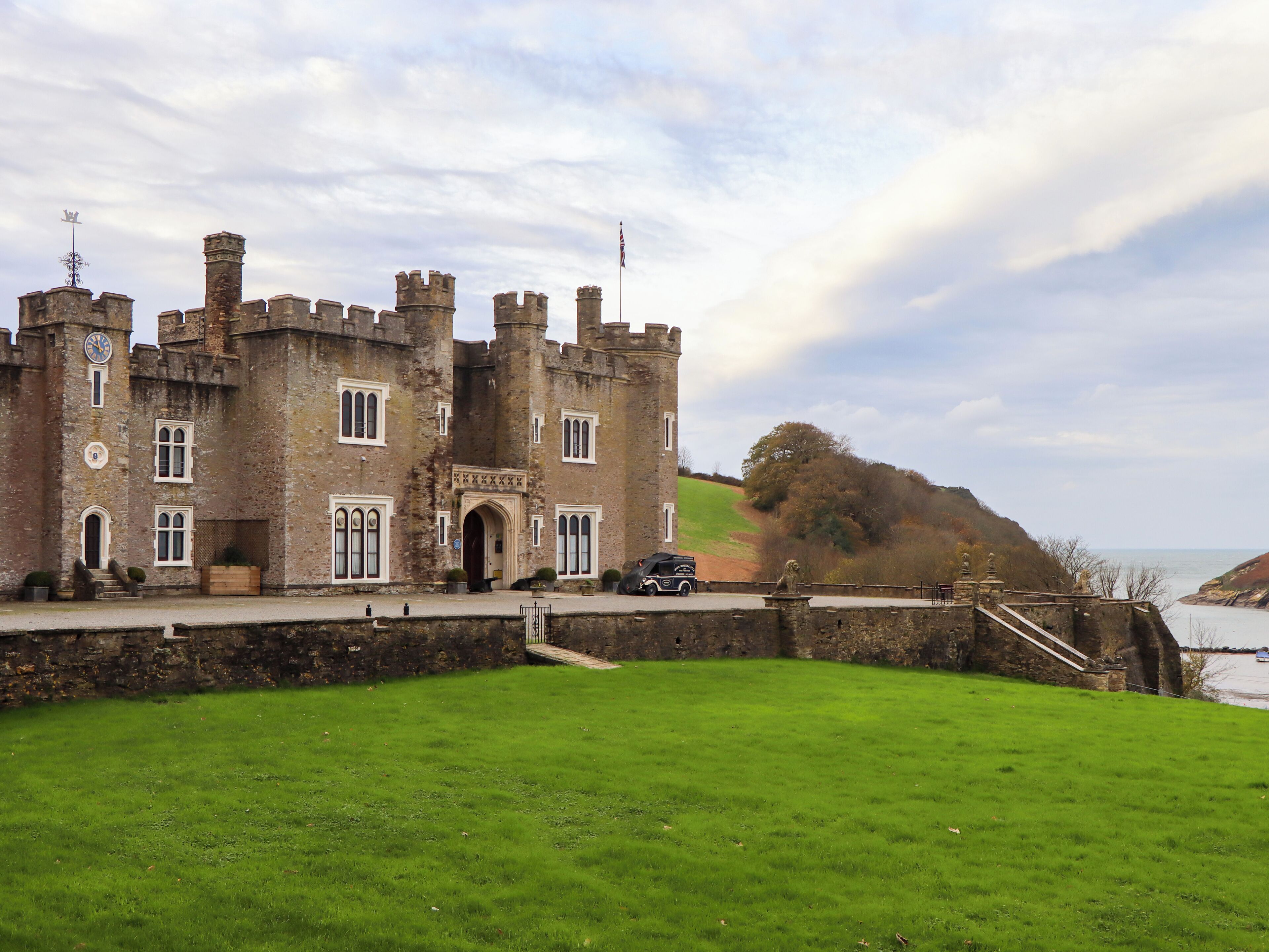 A historic castle with a large lawn in front, a paved entrance, and a view of the sea.