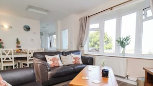 A modern living room with a leather sofa, a wooden coffee table, and a view of the outdoors through large windows. - Castle View Lodge (Ilfracombe)