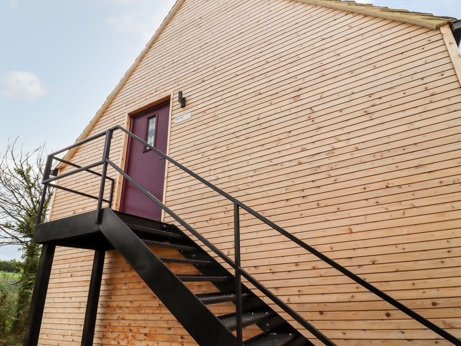 Un edificio de madera con una puerta morada y una escalera negra que lleva a una plataforma.