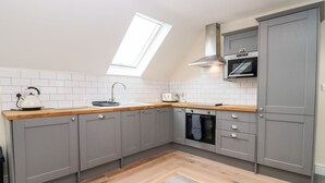 A modern kitchen with grey cabinets, a wooden countertop, a skylight, and a built-in oven. - Bears Court The Flat (Cheltenham)