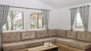 A modern living room with a sectional sofa, a wooden coffee table, and large windows with patterned curtains. - 6 Manor Park (Bideford)