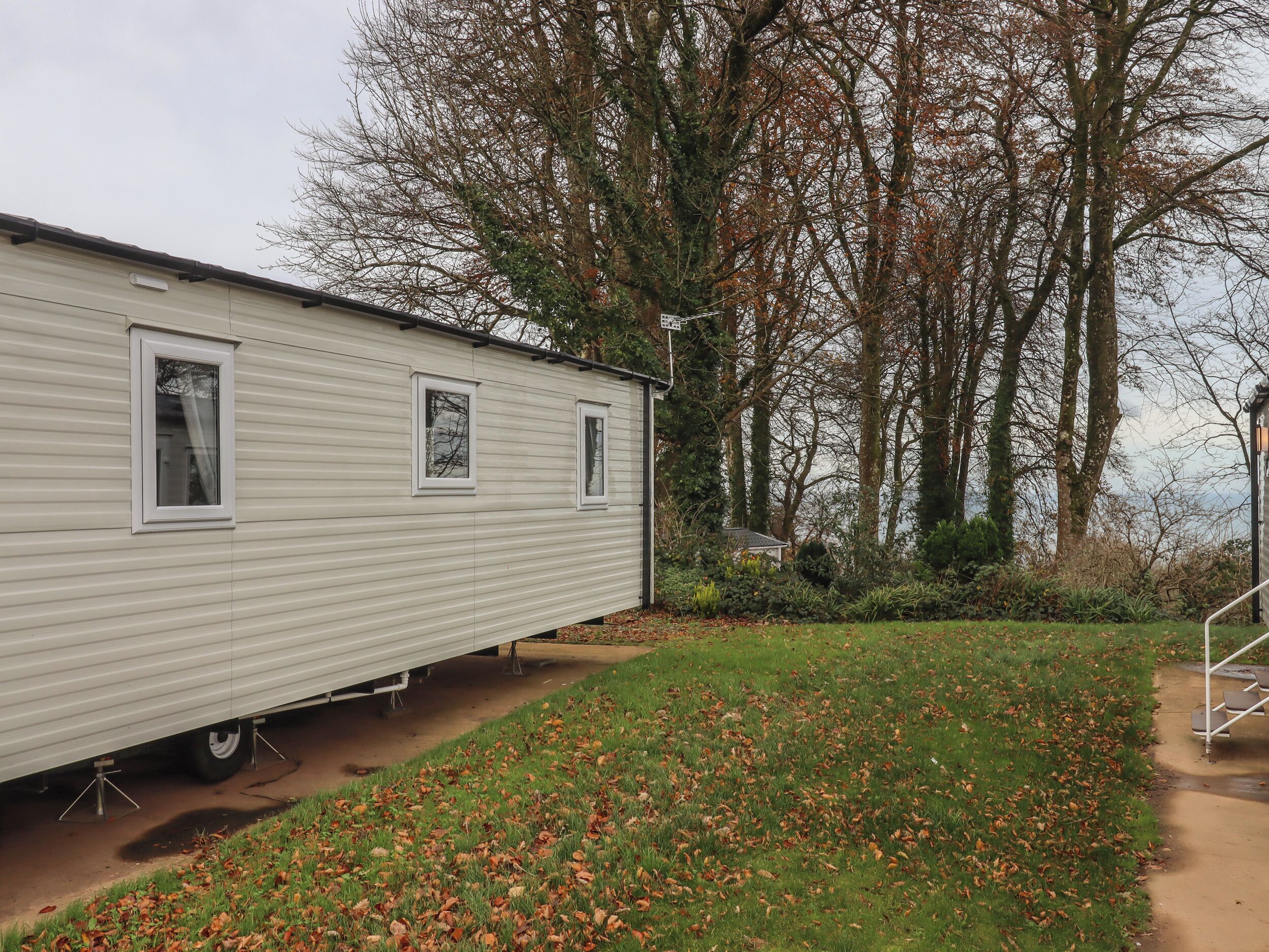 A mobile home with a small porch area, surrounded by trees and a grassy yard.