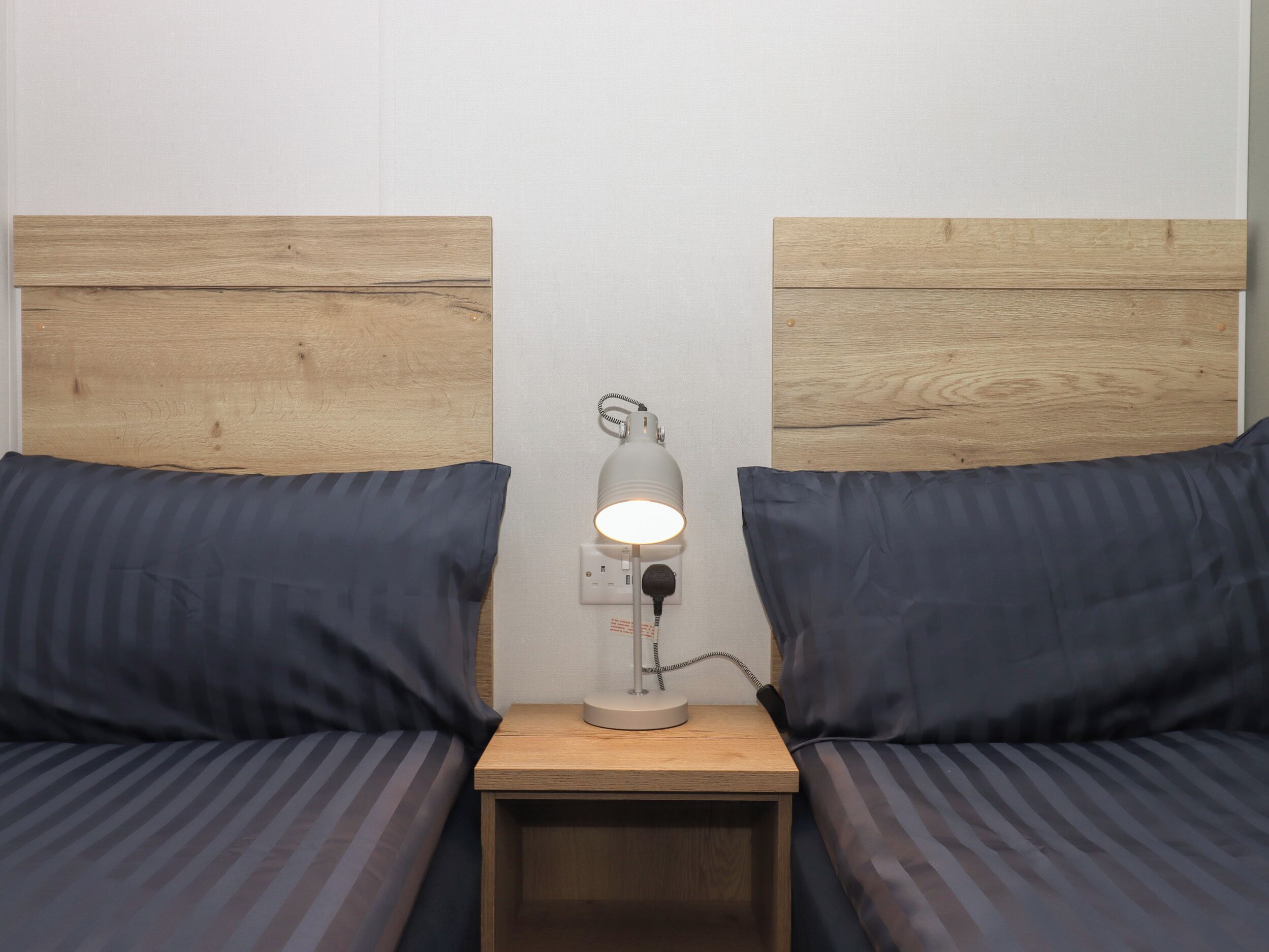 Un lit double avec une literie bleu foncé, une table de chevet avec une lampe et des têtes de lit en bois.