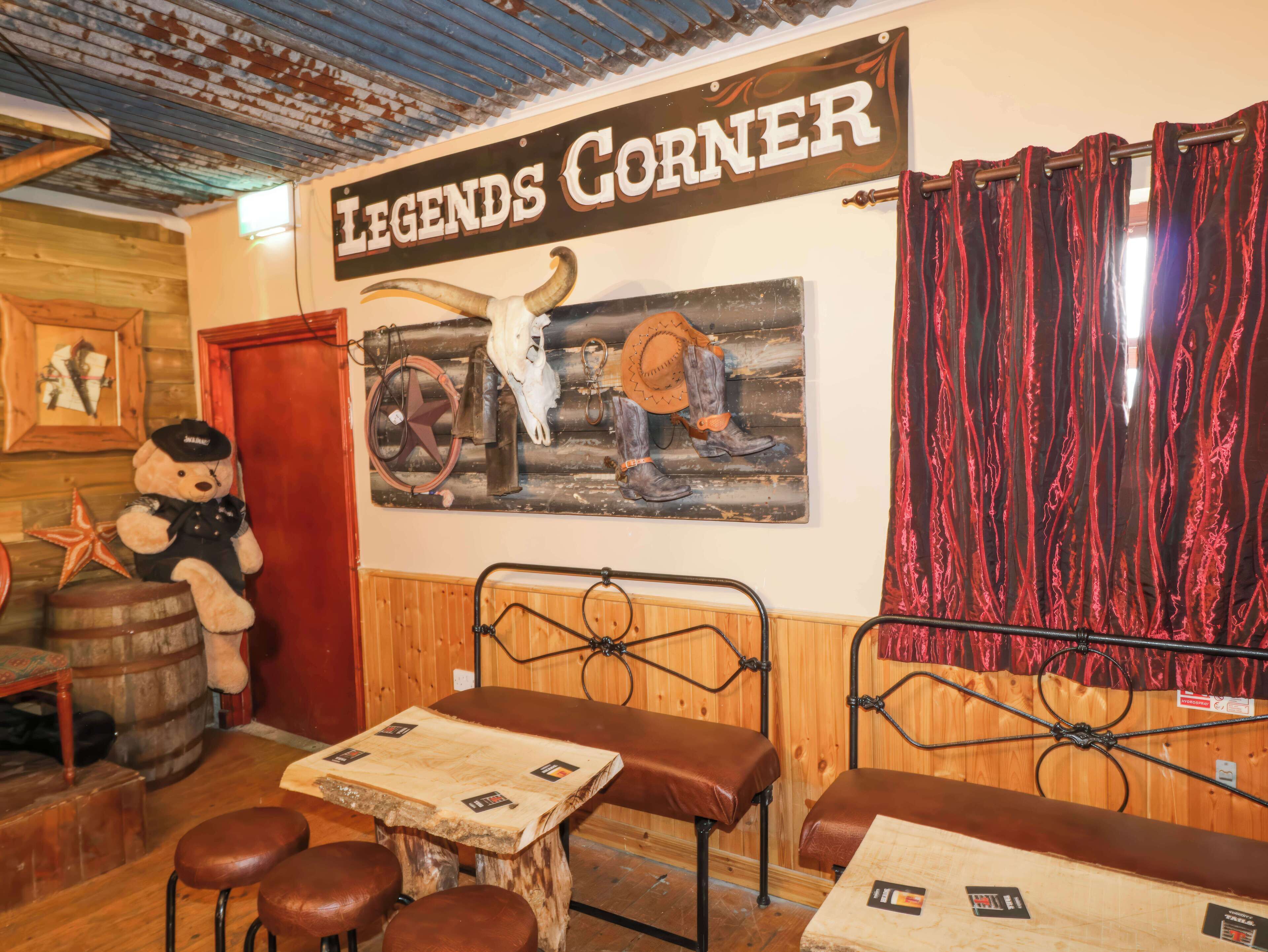 Interior de restaurante de estilo rústico con paredes de madera, una mesa de madera, bancos de cuero y un letrero que dice 'LEGENDS CORNER'.