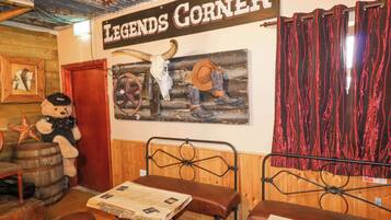 Interior de restaurante de estilo rústico con paredes de madera, una mesa de madera, bancos de cuero y un letrero que dice 'LEGENDS CORNER'.