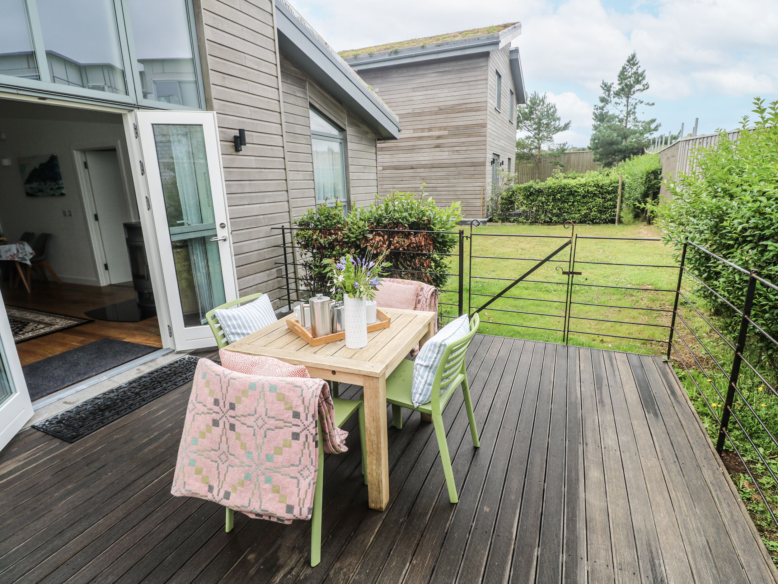 Eine Holzterrasse mit Tisch und Stühlen, einem Blumentopf und Blick auf ein Haus mit einer Schiebetür.