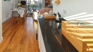 A modern kitchen with a black countertop, wooden cabinets, and a dining area with a table and chairs. - Una, Lodge 70 (St Ives)