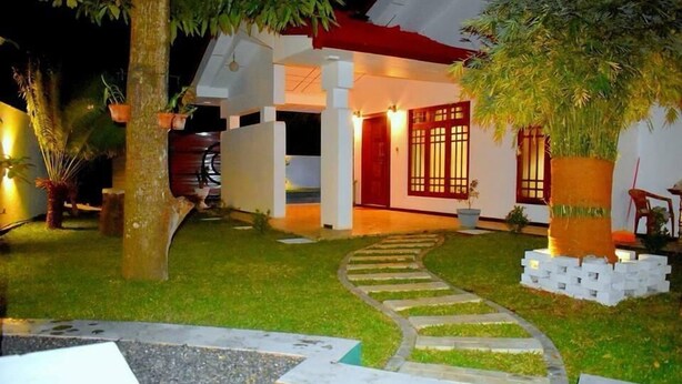 Una casa con un sendero que lleva a la entrada, rodeada de follaje y plantas en macetas.