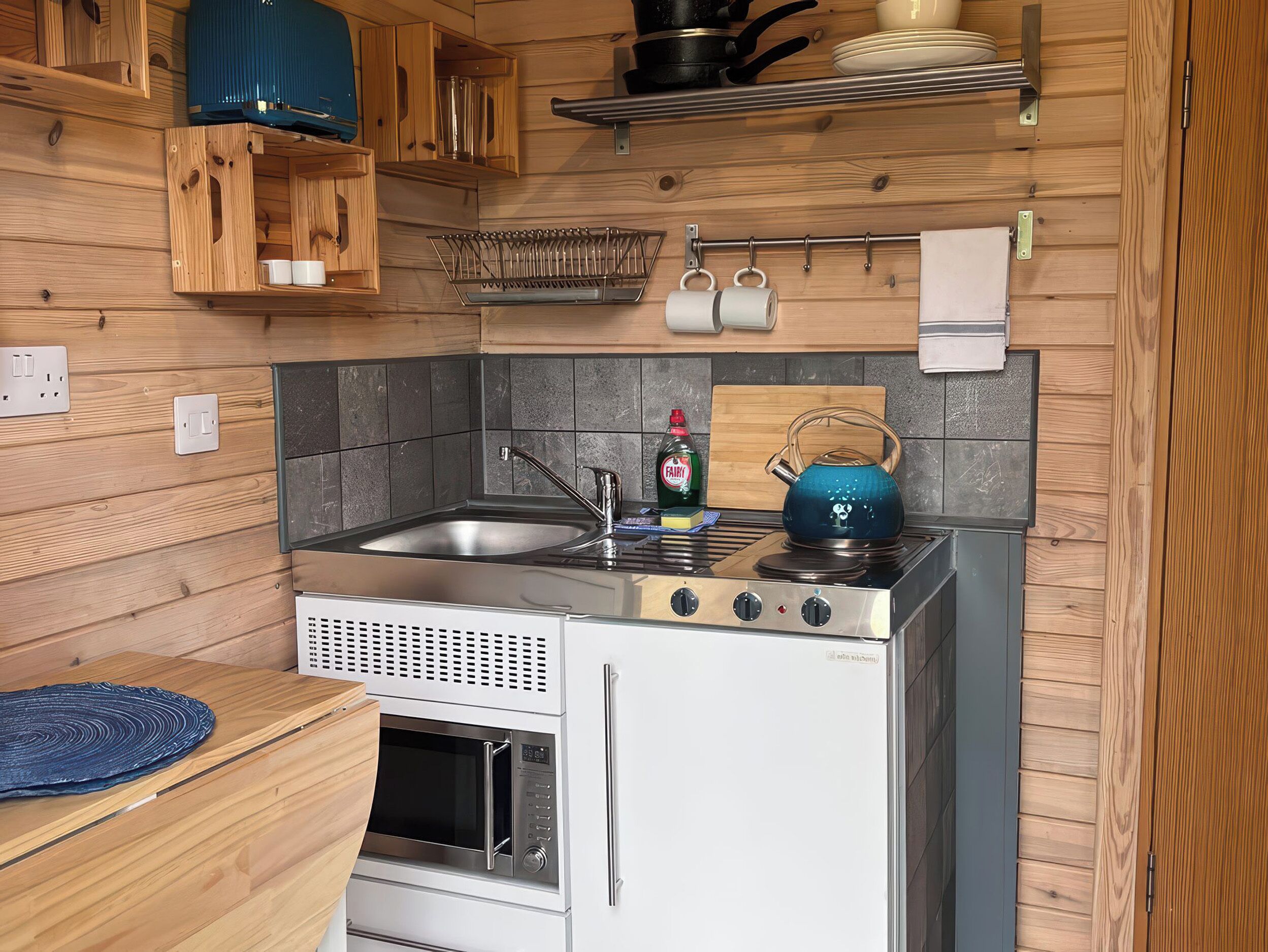 Una cocina compacta con armarios de madera, estufa integrada, microondas y pileta.