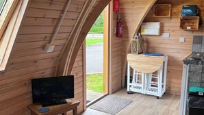 A cozy cabin interior with a wooden interior, a television on a small table, a kitchen area with a stove, and a fire extinguisher. - Lakeside Pods - Pets Welcome (Oldham)