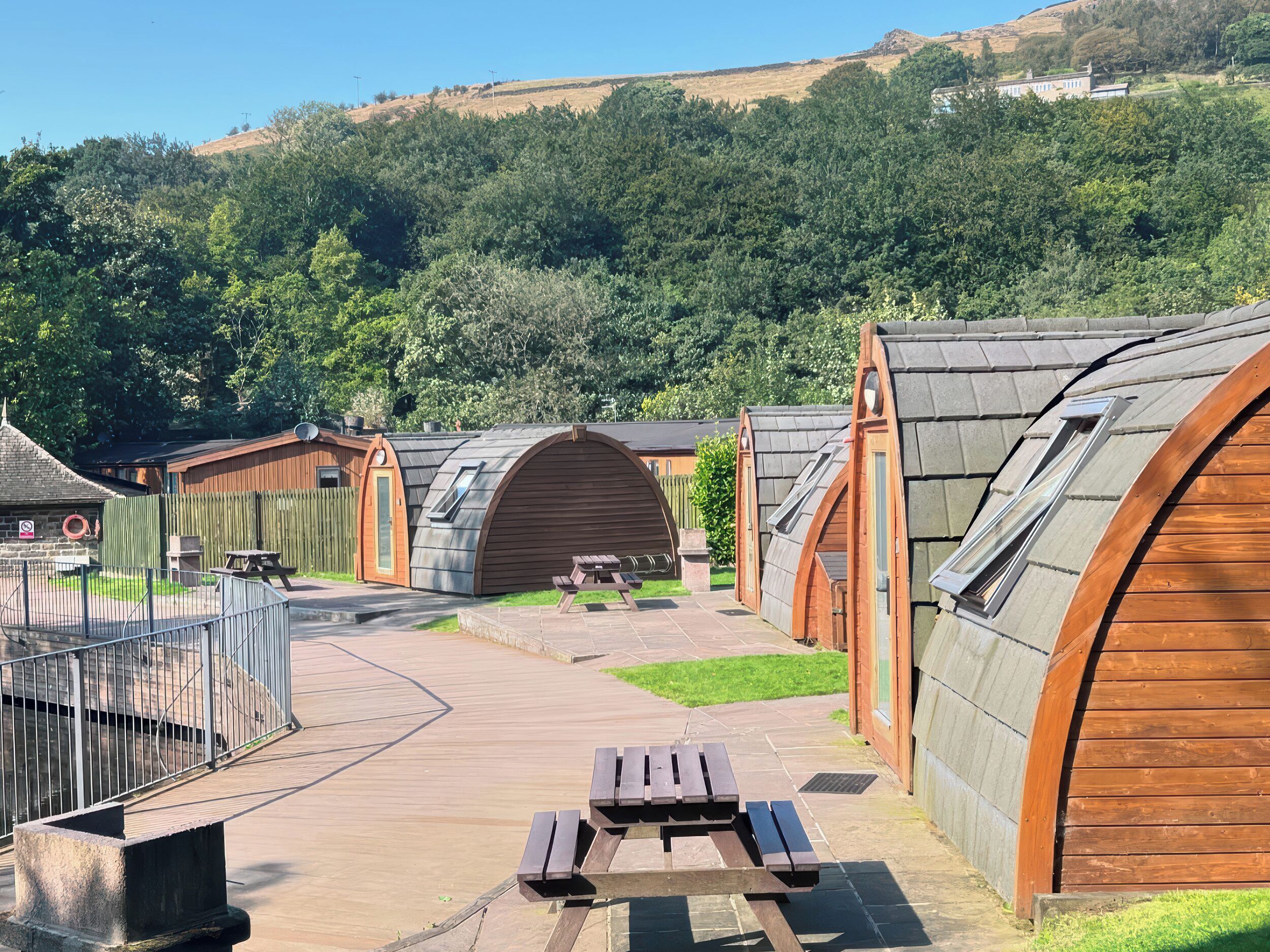 Fileira de cabanas de madeira com telhados inclinados, mesa de piquenique e área cercada com um banco.