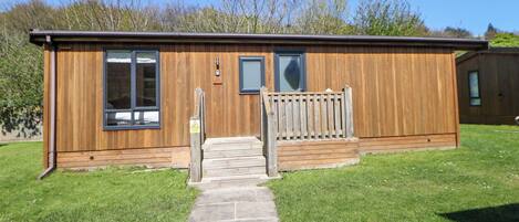 Une cabane en bois avec un chemin de pierre menant à l’entrée, une petite fenêtre et une porte.