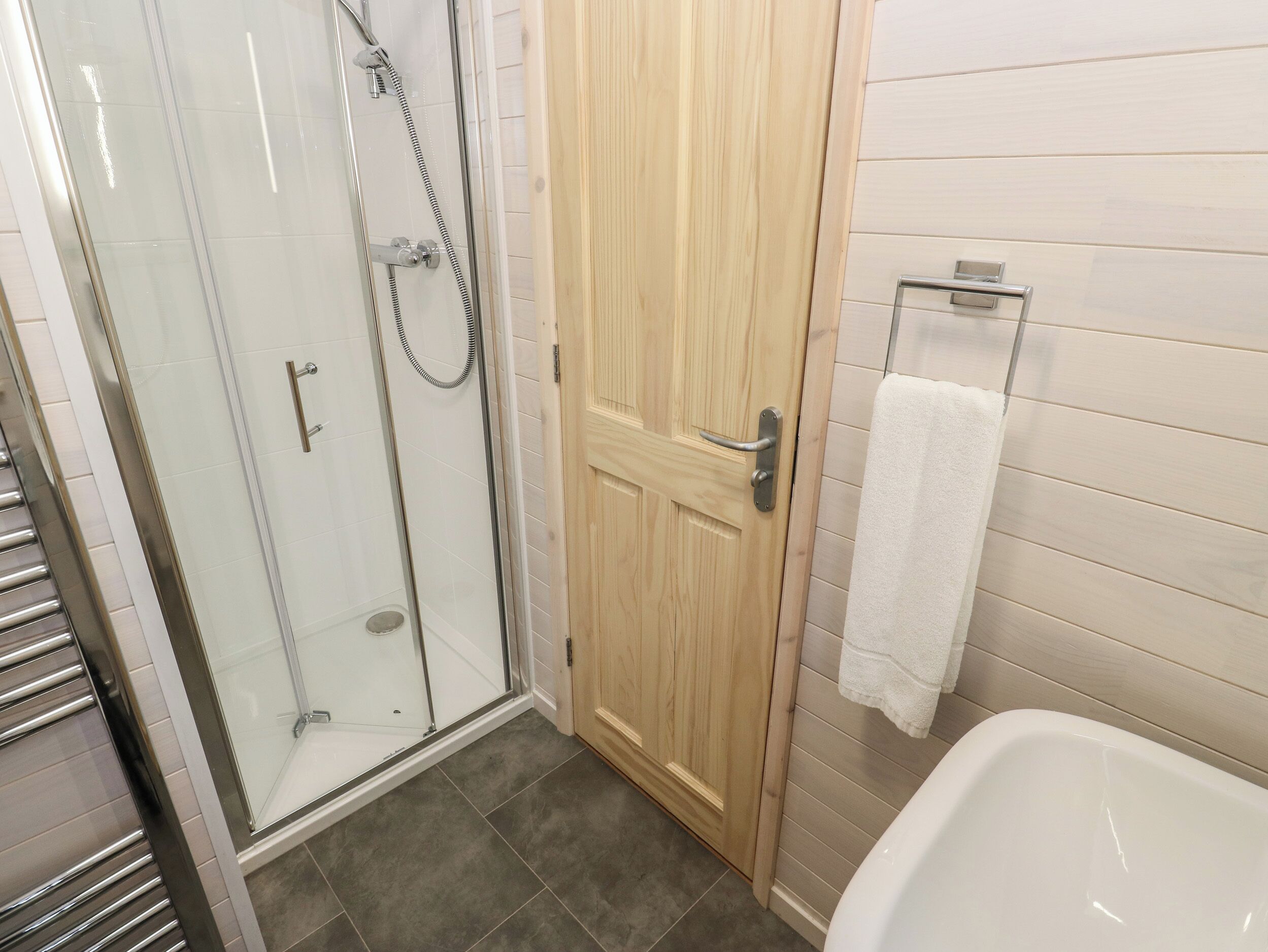 Ein Badezimmer mit Duschkabine, Holztür und weißer Badewanne.