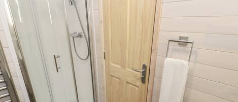 A bathroom with a glass-enclosed shower, a wooden door, and a white bathtub.