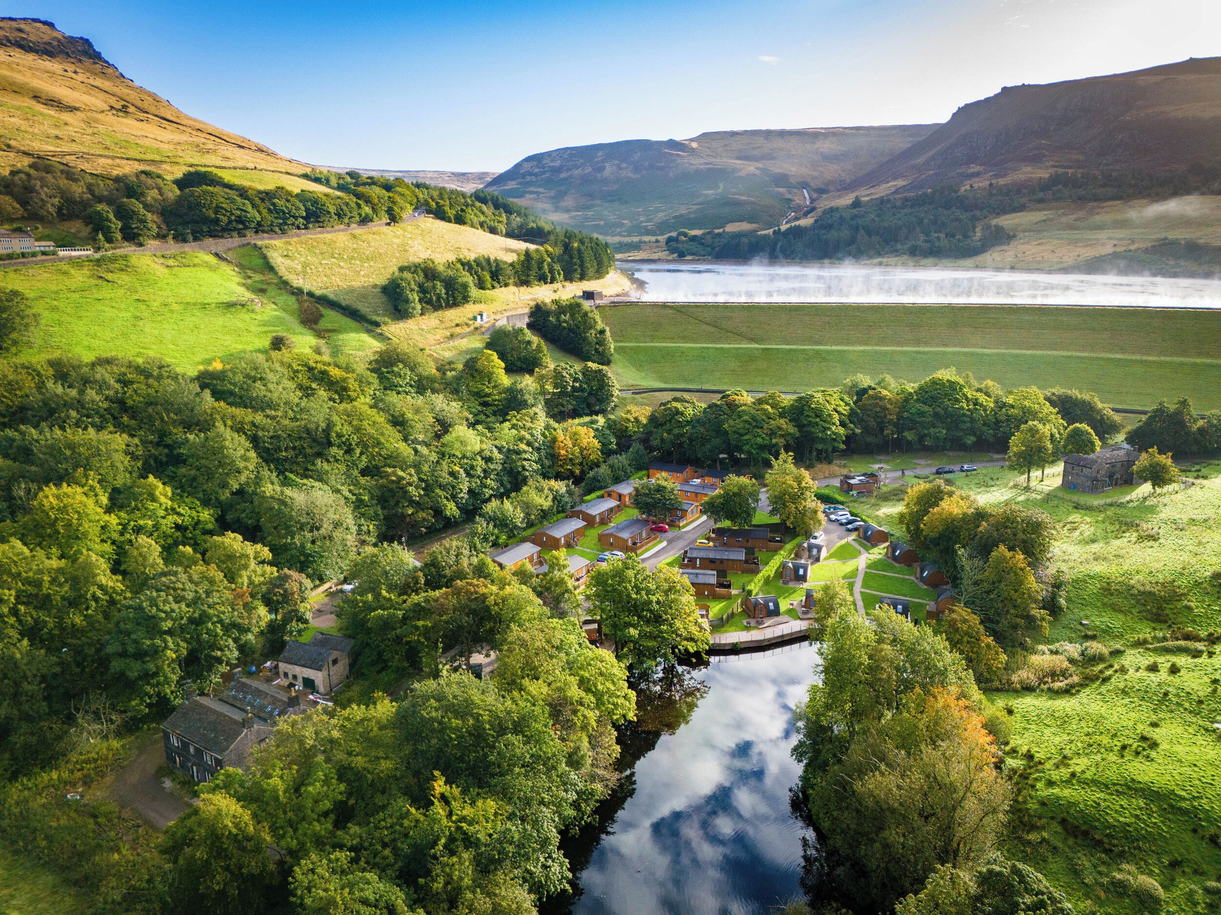 A rural village with a river, surrounded by hills and greenery.