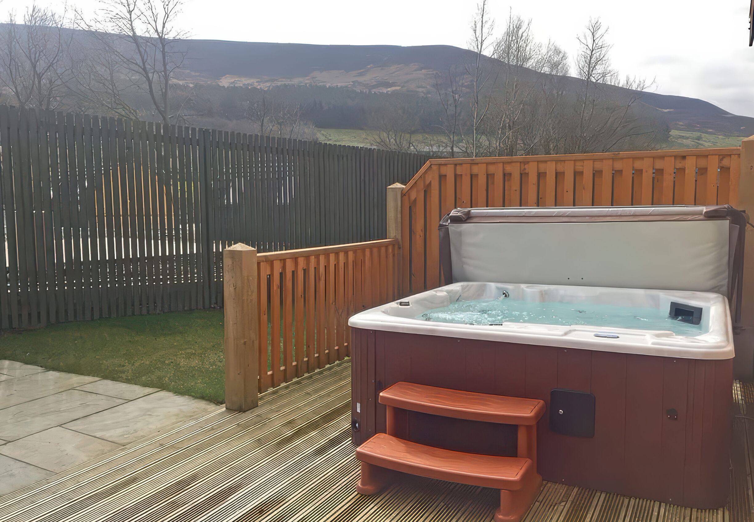 A hot tub on a wooden deck with a view of a mountain and a wooden fence in the background.