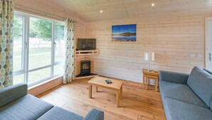 Een gezellige woonkamer met een houten plafond, een open haard, een televisie en een groot raam met gordijnen.