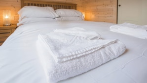 Een netjes opgemaakt bed met witte lakens en handdoeken, een houten hoofdbord en een bedlampje.