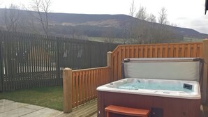 A hot tub on a wooden deck with steps, surrounded by a wooden fence and a grassy area. - Dovestone Luxury Lodges - Pets Welcome (Oldham)
