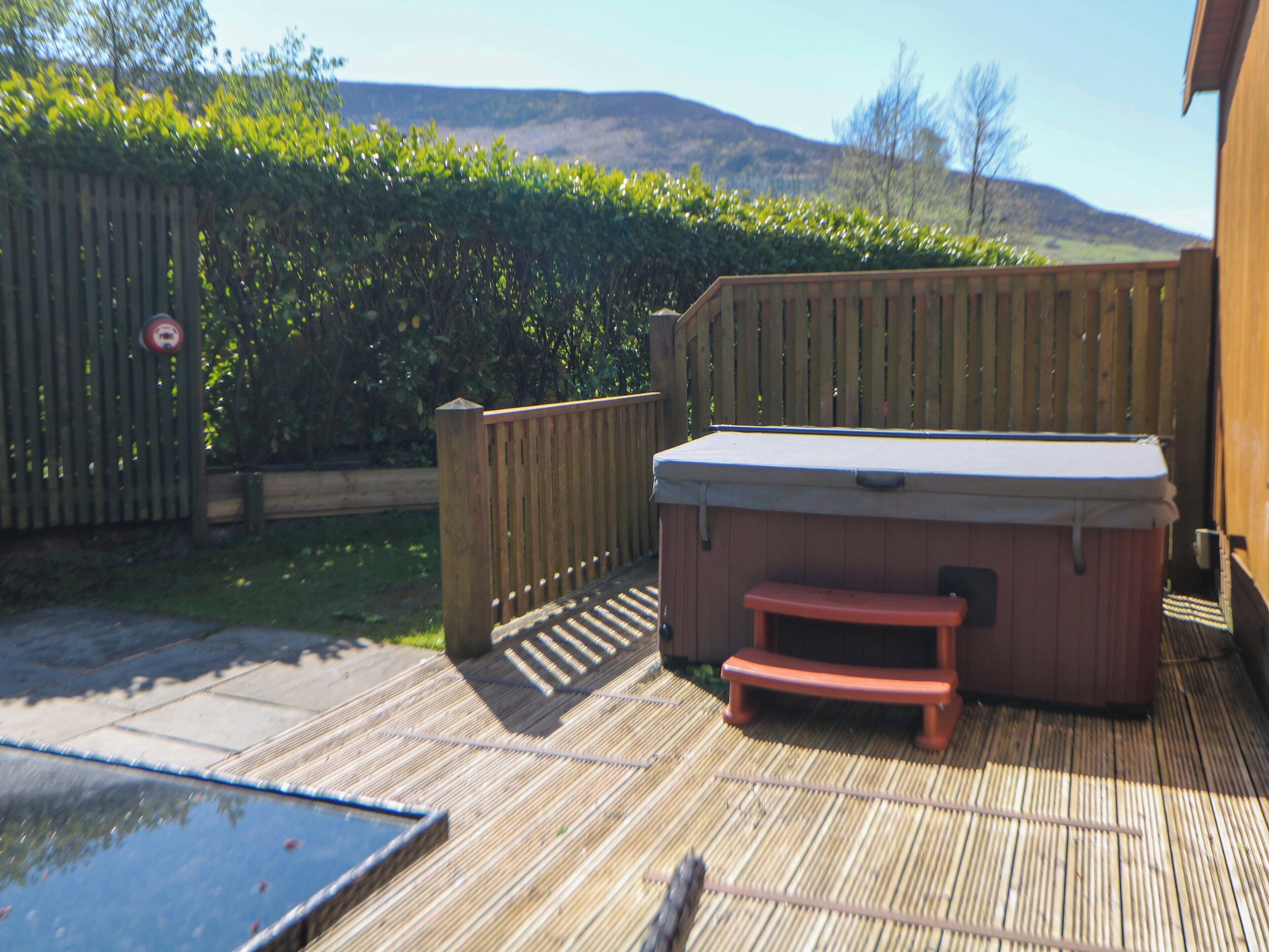 A hot tub on a wooden deck with a wooden fence and a hedge in the background.