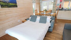 A cozy room with a wooden bed, a dining table with chairs, and a kitchen area with a sink and cabinets. - Dovestone Luxury Lodges - Pets Welcome (Oldham)