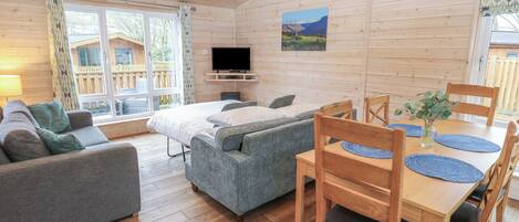 A cozy room with a bed, two sofas, a dining table with chairs, a TV, and a window with curtains.