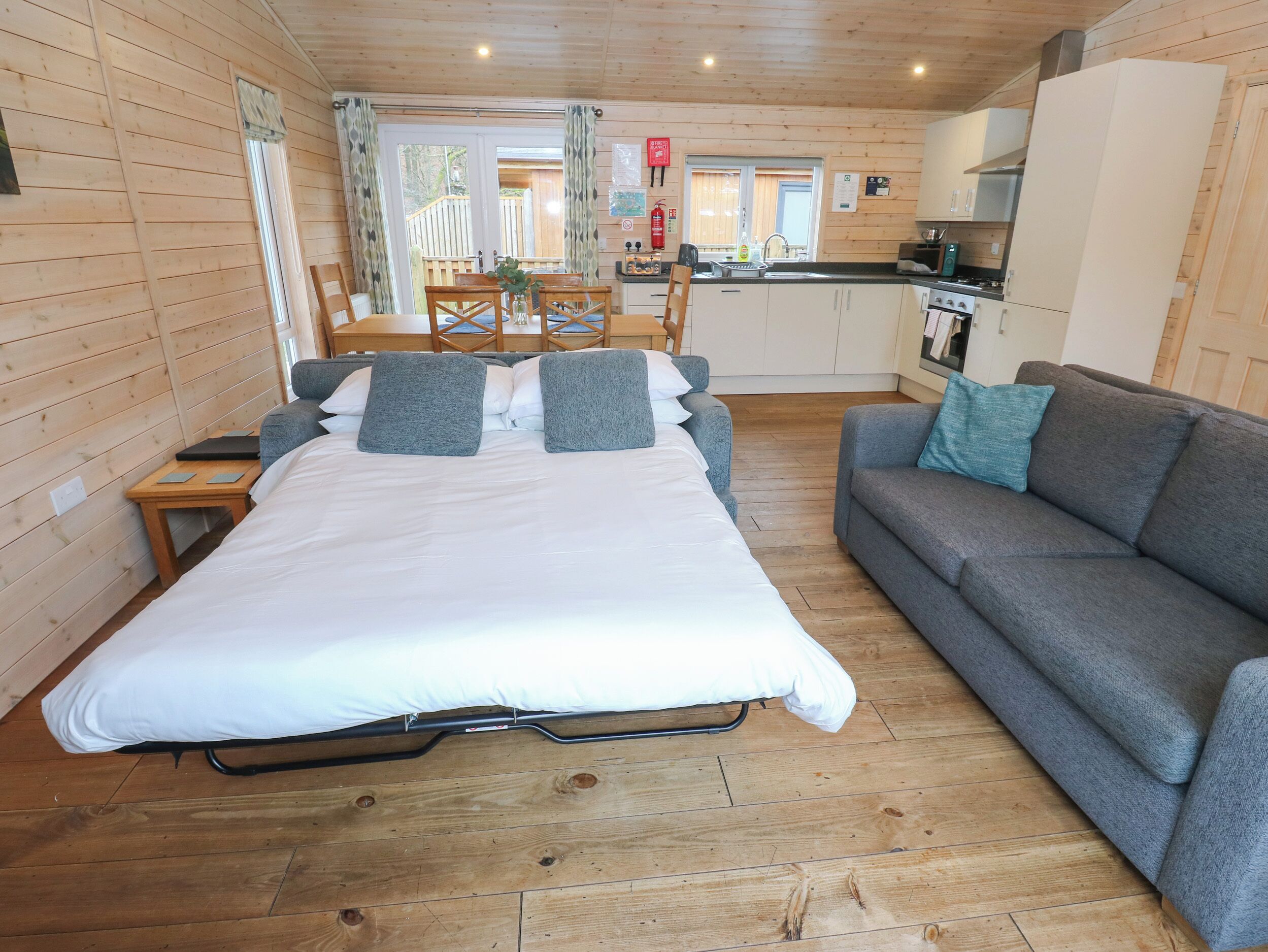 A room with a bed, a sofa, a dining table, and a kitchen area.